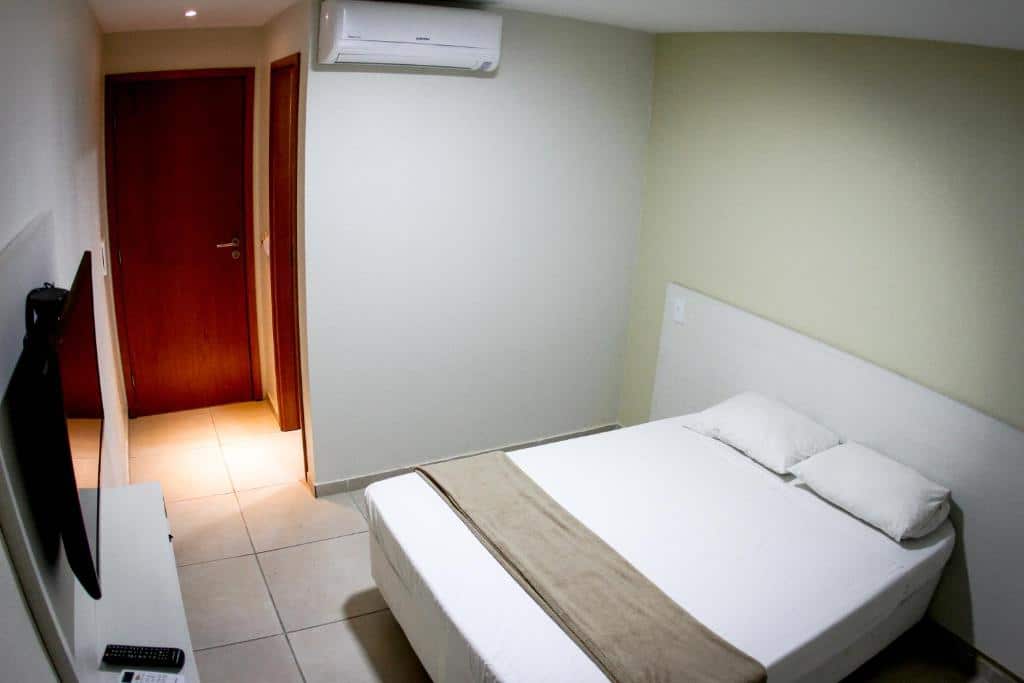 Quarto do Rota 232 Hotel Caruaru. A cama está no lado direito, em frente a cama há um móvel com uma TV e dois controles e no lado esquerdo estão duas portas. Imagem para ilustrar o post hotéis em Caruaru.