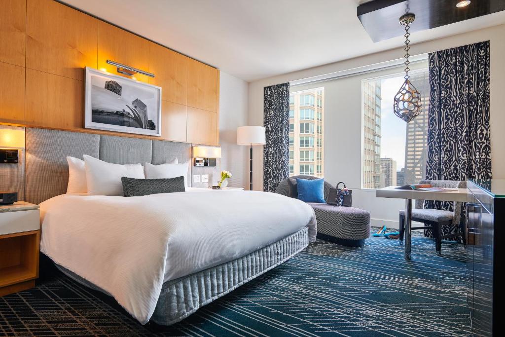Quarto do Sofitel Chicago Magnificent Mile com cama de casal, duas cômodas de brancas ao lado da cama, do lado esquerdo sofá cinza perto da janela e mesa de trabalho.
