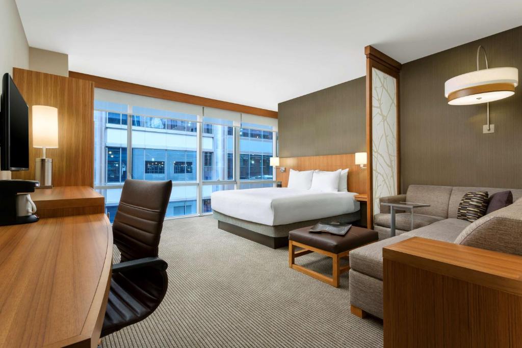 Quarto no Hyatt Place Chicago/Downtown com uma cama king-size, escrivaninha, cadeira de escritório, sofá, janela grande e decoração moderna.