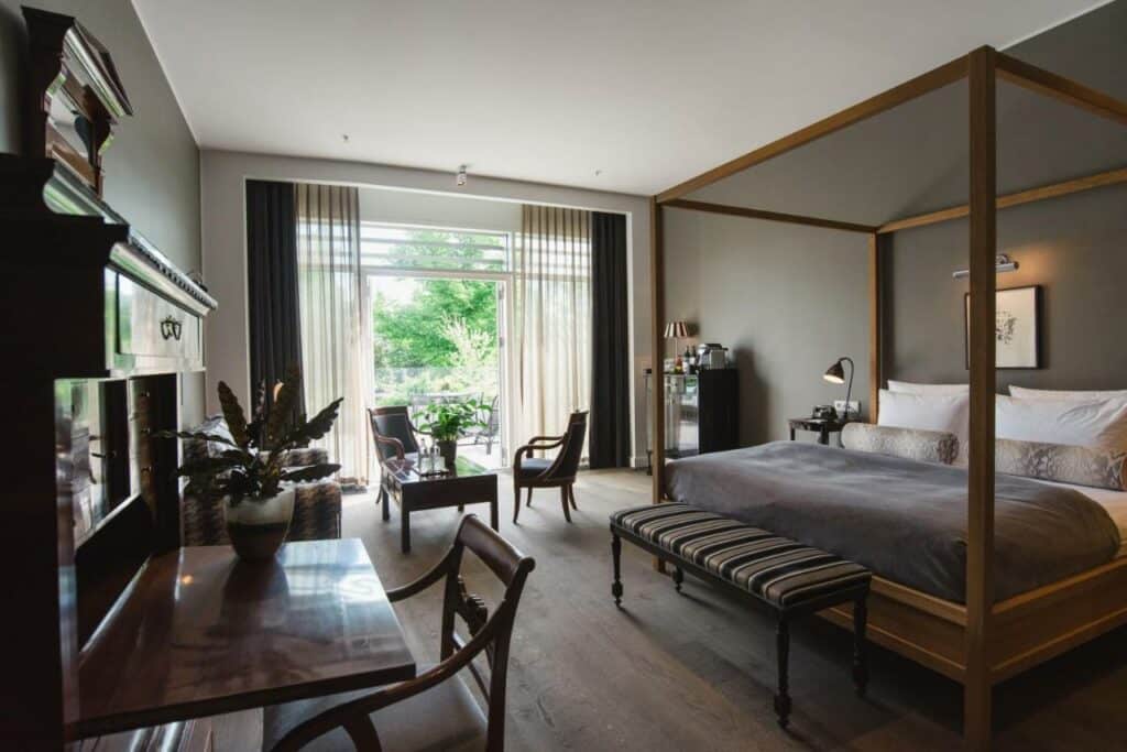 Quarto do Nimb Hotel com uma cama grande de casal com pergolado e um recamier. Há também duas mesas, cadeiras, armário, vasos de planta e uma varanda com cortina. Foto para ilustrar post hotéis em Copenhague.