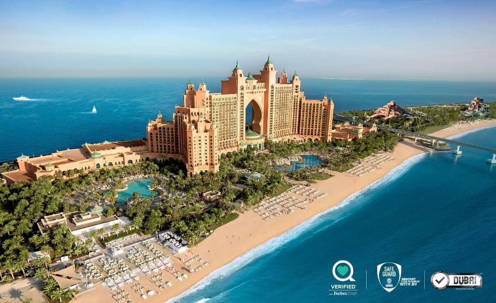 Vista aérea do hotel Atlantis, The Palm, em Dubai, cercado por piscinas, palmeiras e uma praia de areia ao longo do oceano.