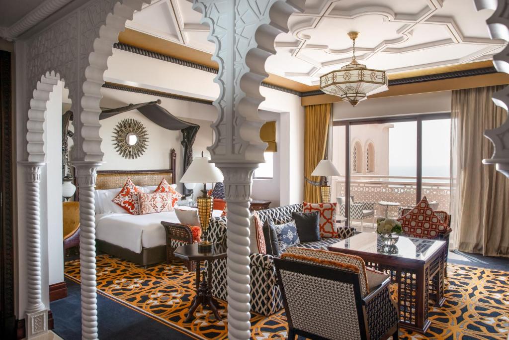 Quarto do Jumeirah Al Qasr com portas em arco, carpete estampado, cama de casal, área de estar, janela grande e varanda com vista.