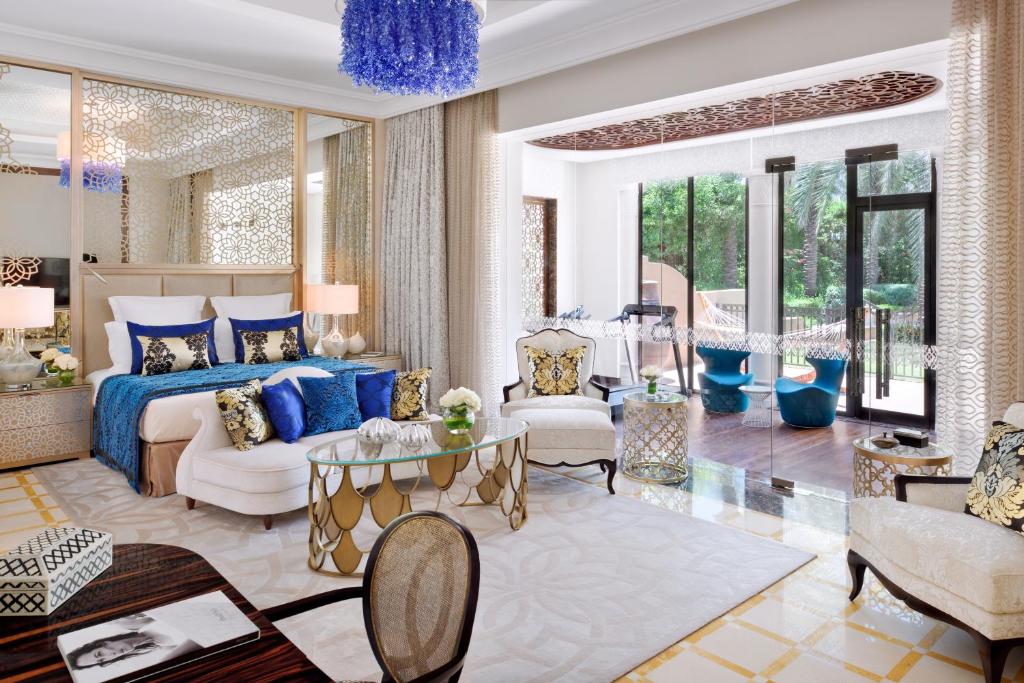 Quarto do One&Only Royal Mirage Resort Dubai, hotel luxuoso com uma cama grande, área de estar elegante, portas de vidro e vista para a vegetação externa.