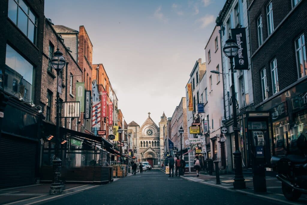 Anne Street em Dublin, com muitas lojas, pessoas andando na rua e uma igreja centralizada ao fim da rua.