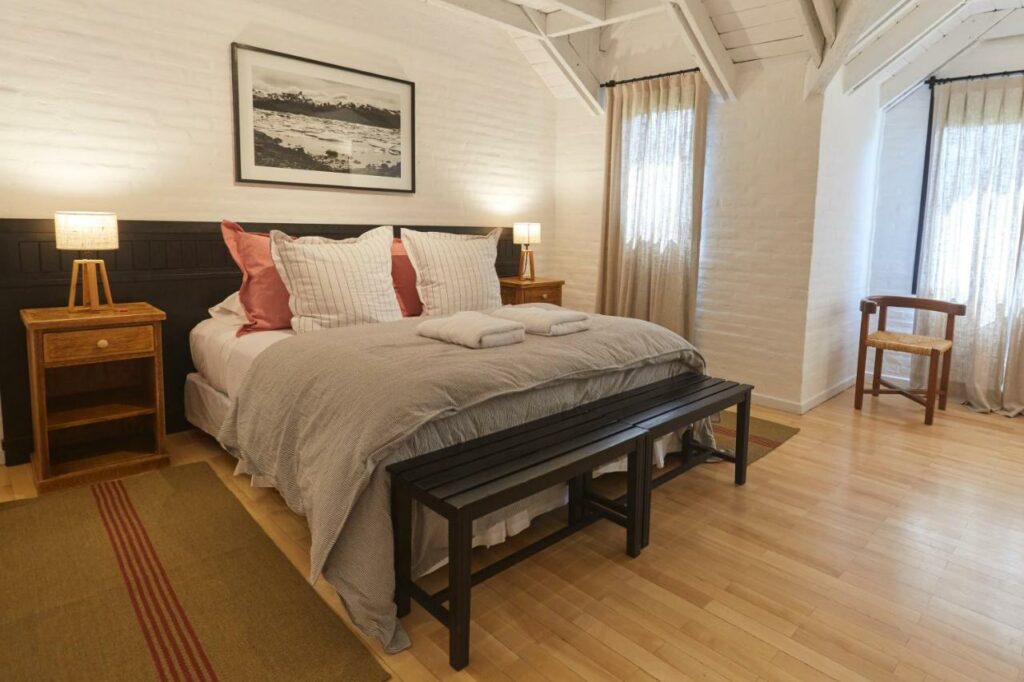 Quarto do Hosteria El Puma com cama de casal do lado esquerdo da imagem com duas cômodas ao lado da cama com luminária, para representar hotéis em El Chalten.