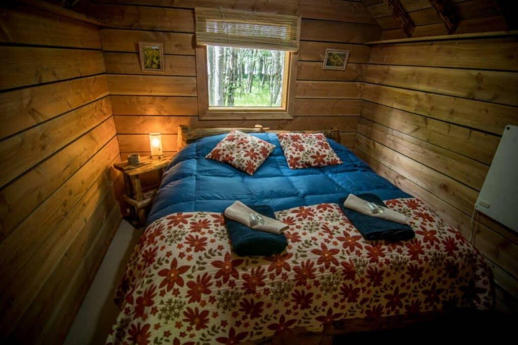Quarto do Laguna Condor – Refugio de Montaña com uma cama de casal no centro com uma cômoda do lado esquerdo da imagem, para representar hotéis em El Chalten.