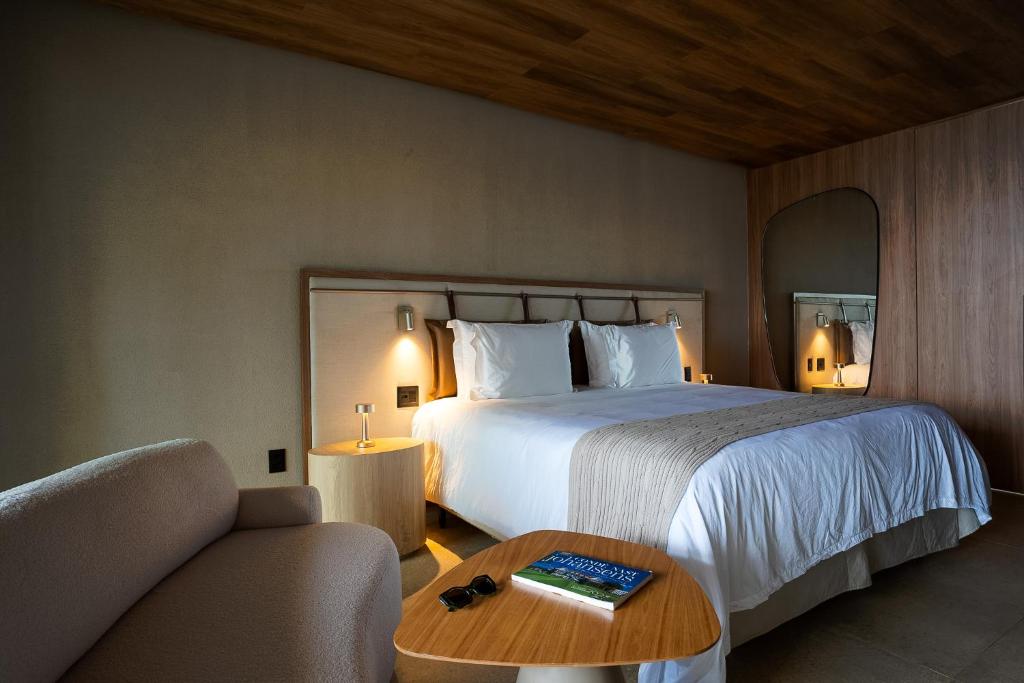 Quarto do Hamares Boutique Hotel. Uma cama de casal e um espelho do lado direito. De cada lado da cama uma luminária e uma mesinha de apoio. Do lado esquerdo um sofá e uma mesa de centro.