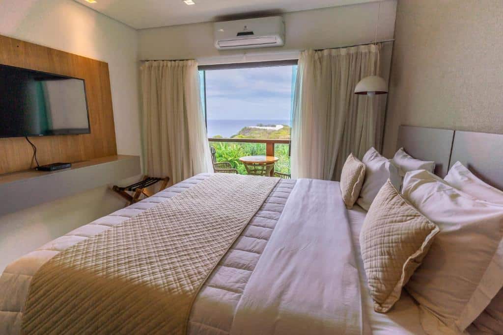 Quarto do Miragem Noronha. Uma cama de casal do lado direito, de frente uma televisão com raque, no fundo a sacada com vista para o mar. Foto para ilustrar post sobre hotéis em Fernando de Noronha.