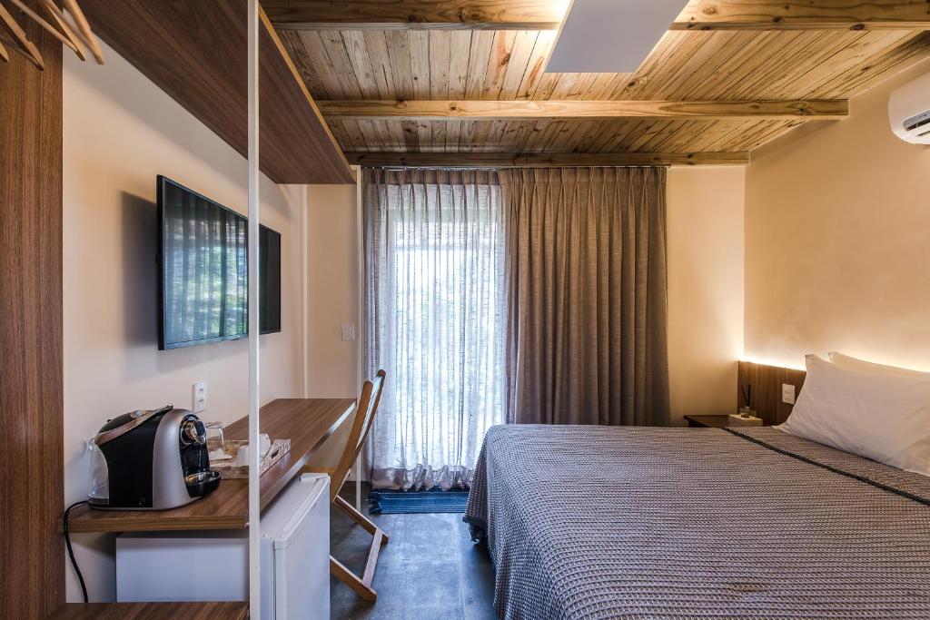 Quarto da Vila Sal Noronha. Uma cama de casal no lado direito, de frente uma mesa com cafeteira, uma cadeira e em baixo um frigobar, e em cima uma televisão. No fundo, a porta com cortina fechada. Foto para ilustrar post sobre hotéis em Fernando de Noronha.