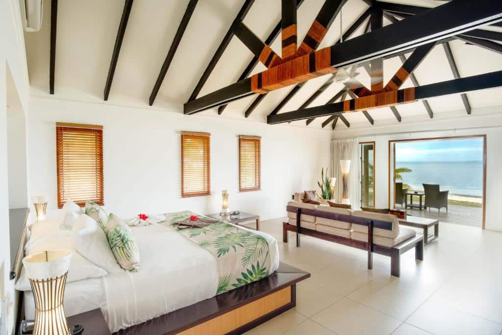 Quarto do Lomani Island Resort – Adults Only  com cama de casal ao centro com duas cômodas ao lado com luminária, em frente uma área de estar com sofá e vista para o mar. 
