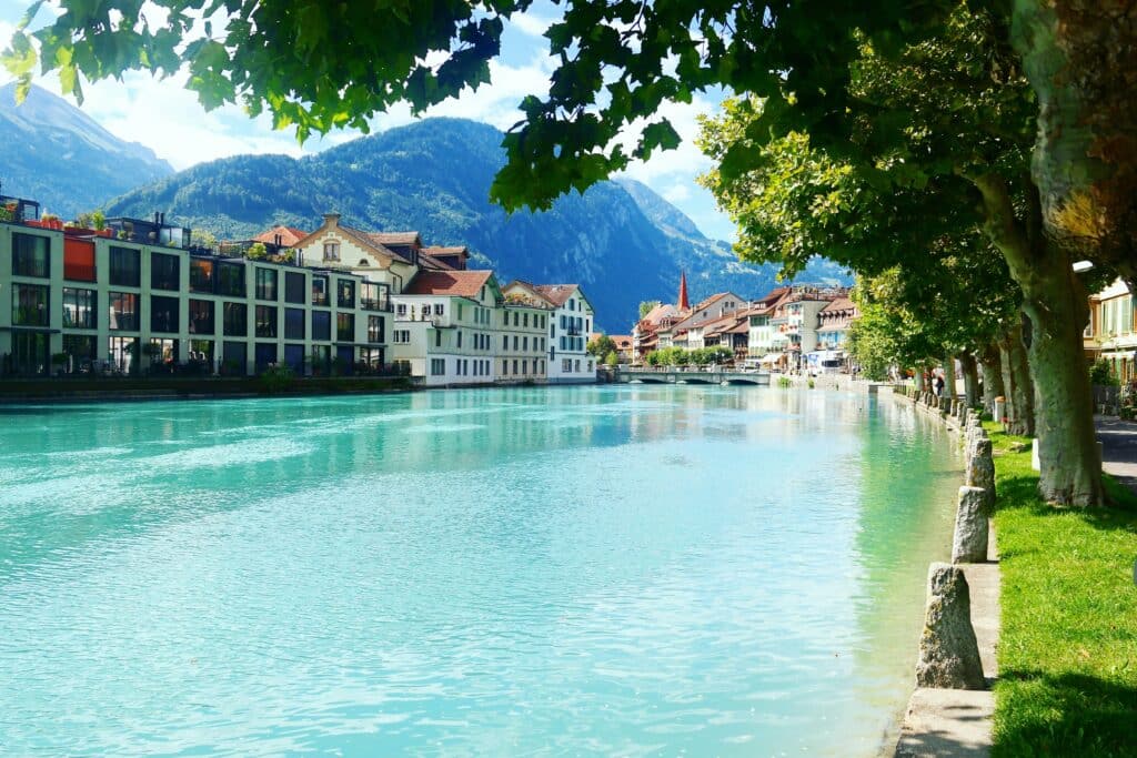 Imagem de um rio a frente no centro em Interlaken durante o dia e do lado direito esquerdo do rio casinhas em estilo alpino.