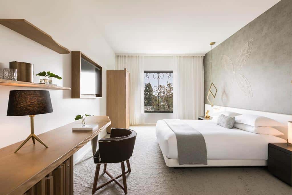 Quarto do Kimpton La Peer Hotel, an IHG Hotel. Do lado direito uma cama de casal, do lado esquerdo uma mesa de trabalho com abajur, uma TV e um guarda-roupa, para representar hotéis em Los Angeles.