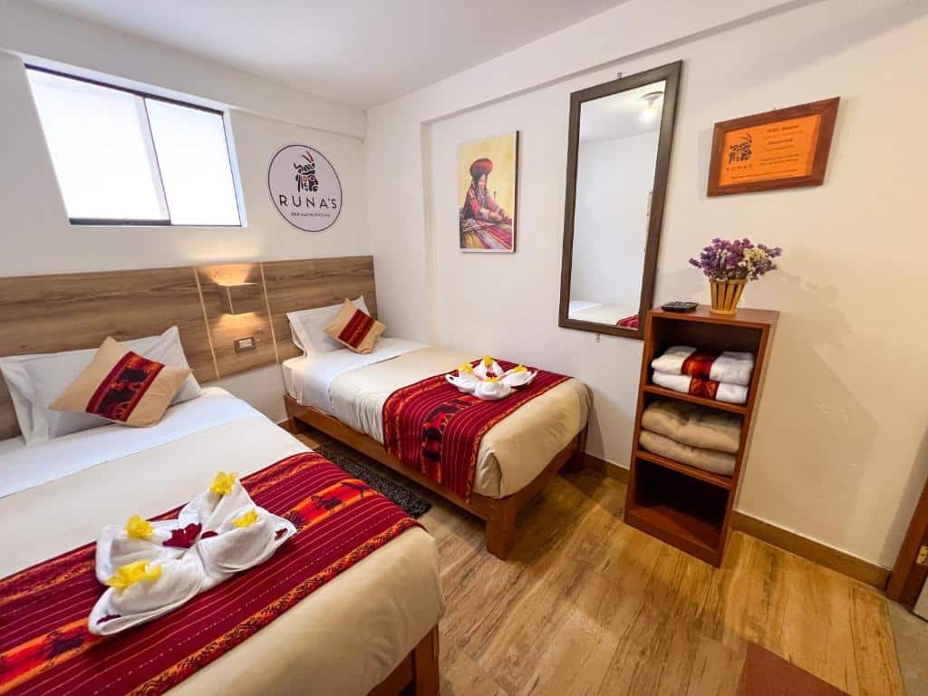 quarto da runas inn machupicchu com duas camas de solteiro, decoradas com toalhas e flores em cima das camas, um espelho vertical preso à parede, no lado direito da suíte, e com uma cômoda com toalhas e um vaso de flores logo abaixo.