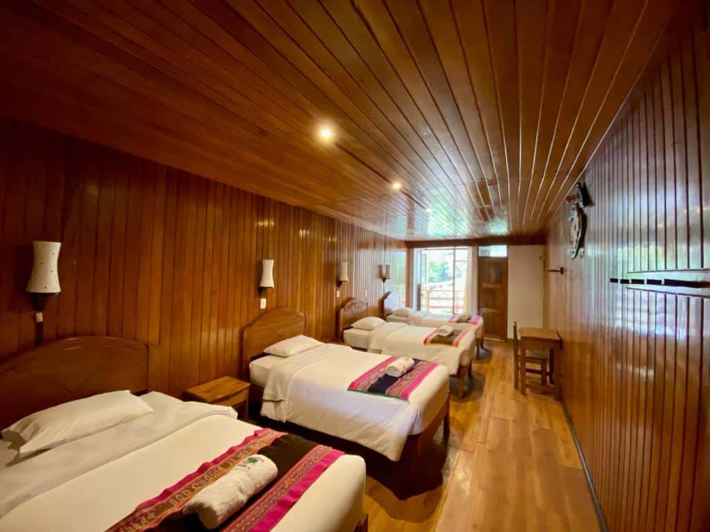 quarto quádruplo do Místico Eco B&B com quatro camas de solteiro, dispostas lado a lado no canto esquerdo da imagem. Todo o quarto é revestido em tábuas de madeira, tanto no chão quanto na parede e no teto.