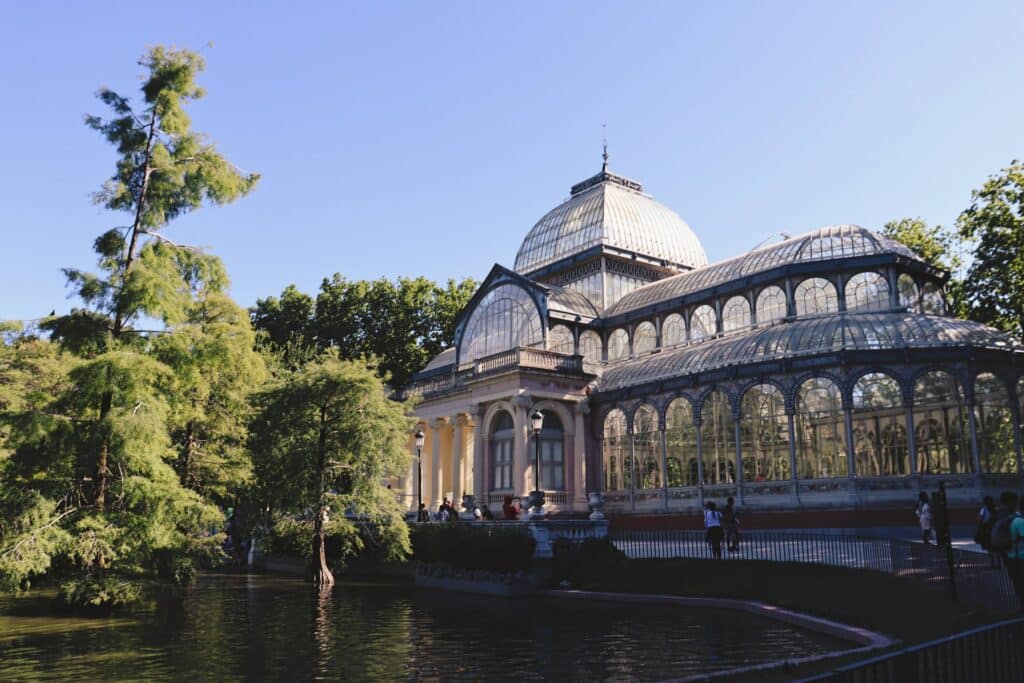 Vista do lago com a estrutura de um palácio de vidro com uma abóbada e plantas ornamentais no Parque de El Retiro em Madri.