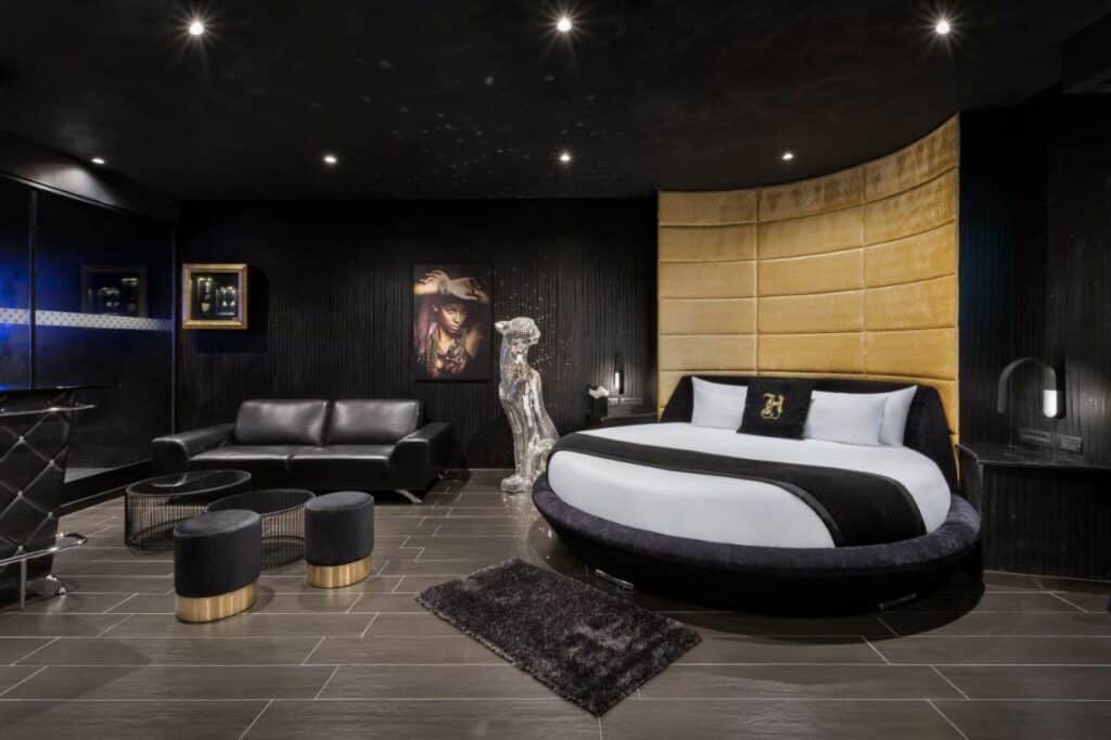 Quarto amplo no H Hotel & SPA - Adults Only em tons de preto e cinza, uma cama redonda, um tapete pequeno, uma sofá de couros preto e alguns itens de decoração, para representar hotéis em Malta