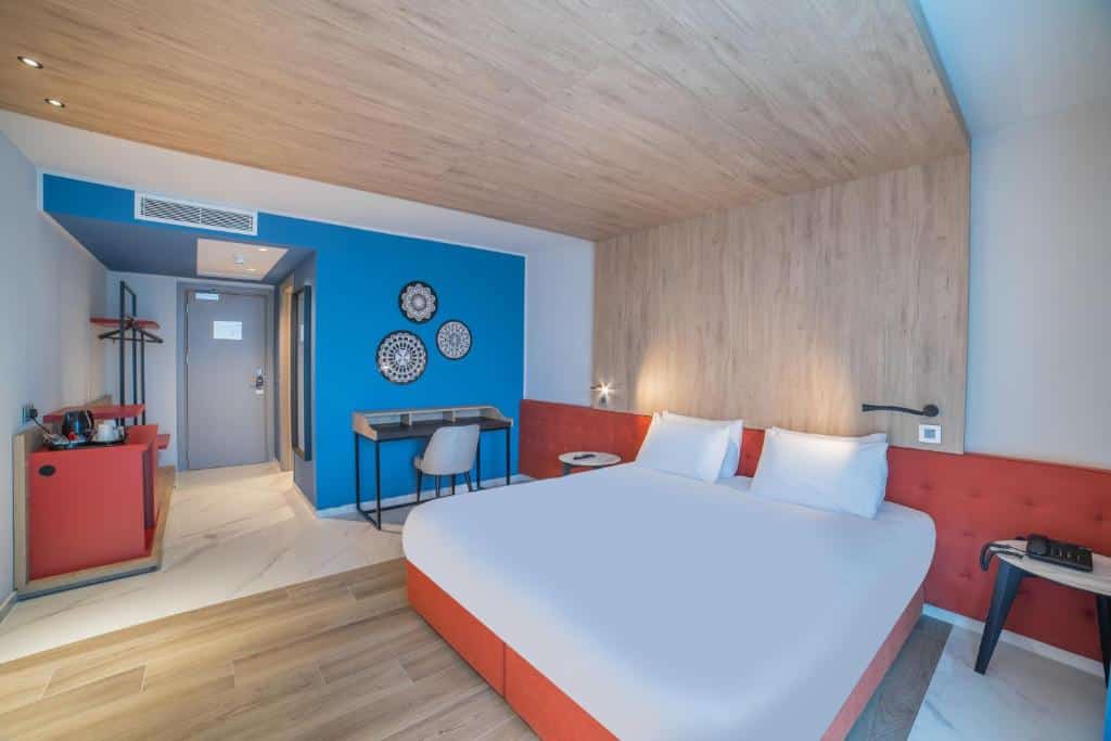 Quarto no Mercure St. Julian's Malta com uma cama de casal, uma mesa de escritório e uma cadeira, um móvel com alguns itens de cozinha, tudo decorado em tons de vermelho, branco e azul