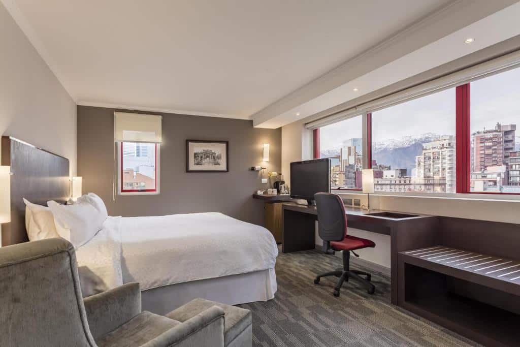 Quarto do Four Points by Sheraton Santiago com cama de casal do lado esquerdo da imagem, em frente a cama uma mesa de trabalho com vista para a cidade. Representa hotéis em Providencia em Santiago.