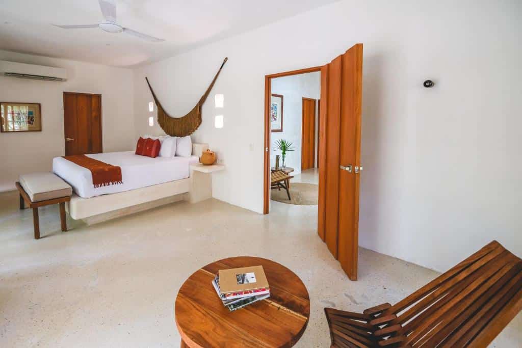 Quarto de Wakax Hacienda, de 94 m², com cama de casal, mesa redonda com uma cadeira de madeira e porta dando acesso a outro cômodo do local, para representar hotéis em Tulum.