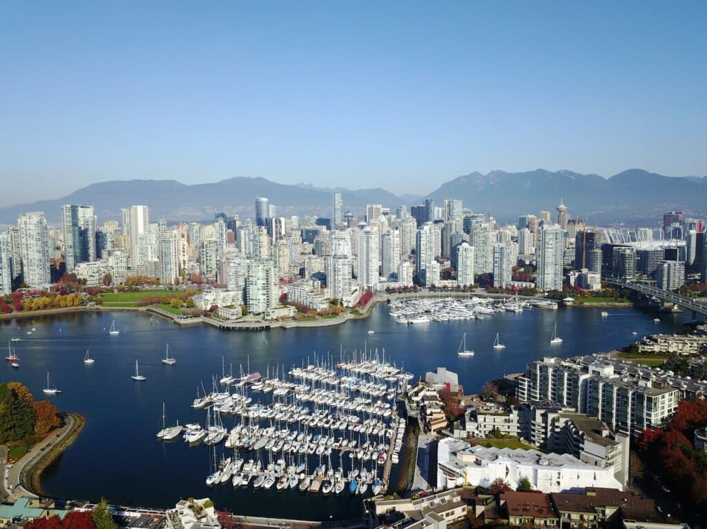 Uma foto aérea da 6th Ave em Vancouver, onde é possível ver uma extensa baía com muitos barcos estacionados e, do outro lado da baía, está a cidade.