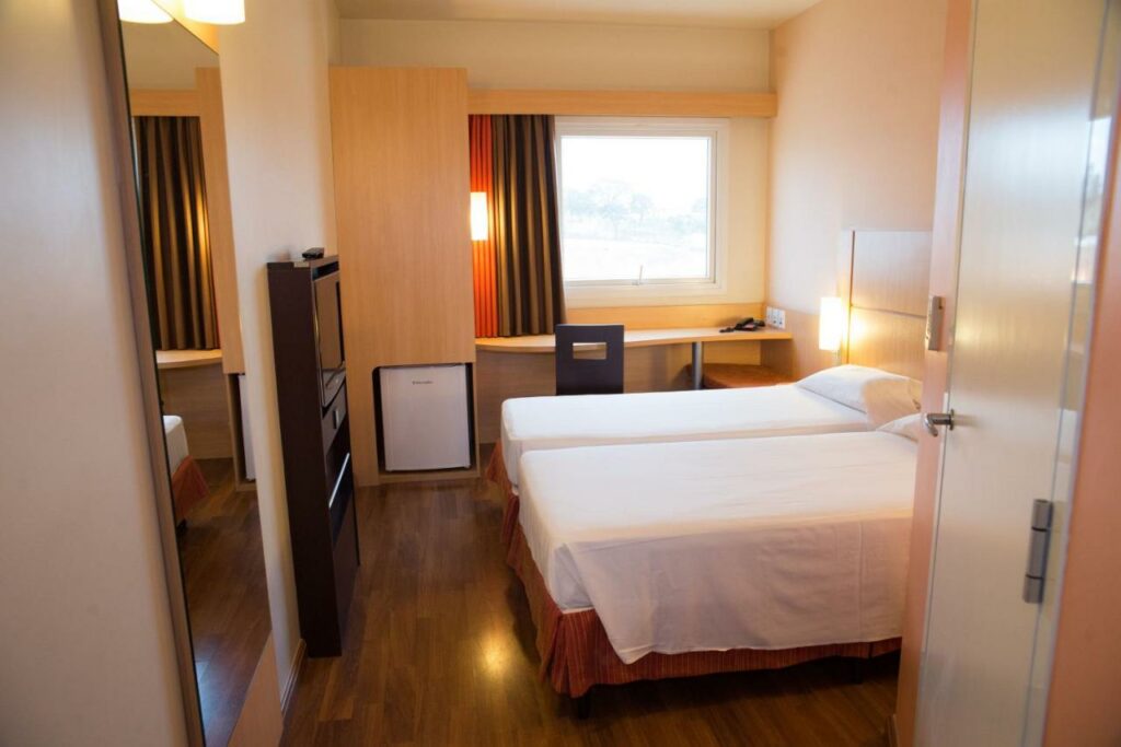 Quarto do Ibis Contagem Ceasa, uma opção além dos hotéis ibis em Belo Horizonte, com duas camas, frigobar, TV, espelho de corpo inteiro, janela com cortina blecaute e mesa de trabalho