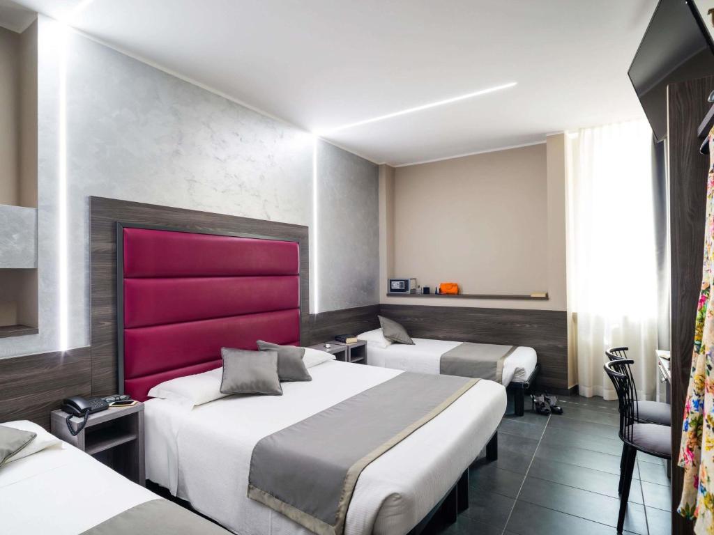 Quarto no Ibis Styles Milano Centro com três camas, roupa de cama cinza e branca, uma cabeceira acolchoada e uma janela com cortinas transparentes, para representar hotéis ibis em Milão.