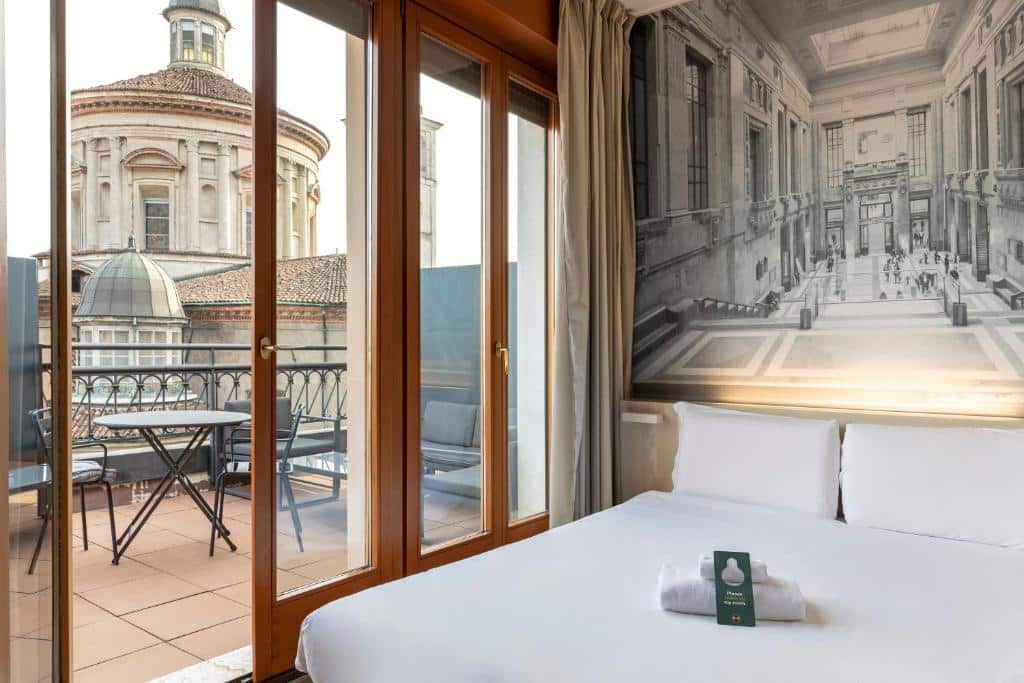 Quarto do B&B Hotel Milano Sant'Ambrogio com um pequeno terraço com uma mesa redonda com cadeiras e um pequeno sofá, dentro, há uma cama de casal com toalhas brancas sob ela