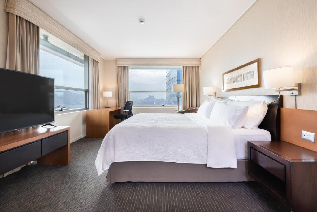 Quarto do Holiday Inn Express Santiago Las Condes, an IHG Hotel com uma cama grande, TV, escrivaninha, duas janelas com vista para a cidade e decoração em cores neutras, para representar hotéis Mercure em Santiago.