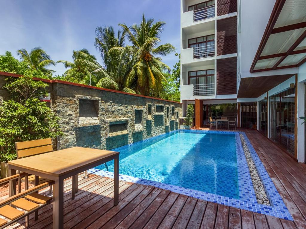 Piscina do Plumeria Maldives, localizada em uma área fechada com um muro de pedras no lado esquerdo, e em volta o chão é todo de madeira. No lado direito tem o prédio do local, que possui pequenas sacadas nos quartos e parede de vidro do andar térreo. Imagem para ilustrar o post de hotéis nas Maldivas
