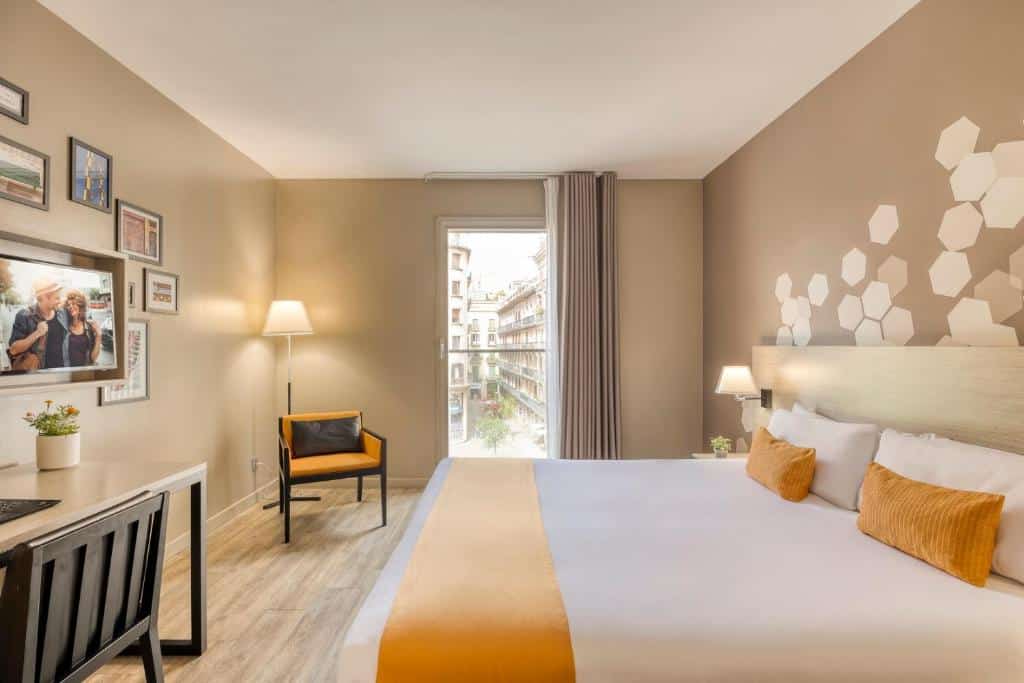 Quarto do Citadines Ramblas Barcelona, uma das recomendações de hotéis nas Ramblas em Barcelona. A cama d casal tem msinhas de cabeceira com abajur dos dois lados ncara uma msa de trabalho com cadeira, vaso de plantas e televisão na parede acima. Ao fundo, uma poltrona e um abajur estão ao lado de uma janela com cortina bege fechadas.
