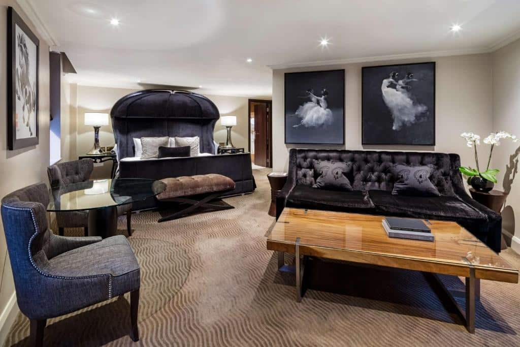 Quarto super amplo do Radisson Blu Edwardian Mercer Street Hotel, London com uma cama de casal com uma cabeceira preta que cria uma espécie de abóboda, há uma mesinha de vidro com duas poltronas, um sofá para três pessoas, uma mesa de centro de madeira, além de alguns itens de decoração 