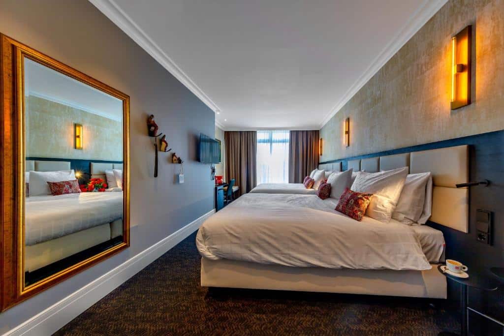 Quarto família do De Ware Jacob Boutique Hotel, de 30 m², com duas camas de casal grande, uma mesa de trabalho, um espelho grande na parede e uma mesinha ao lado da cama com uma xícara em cima. Representa hotéis para família em Amsterdam
