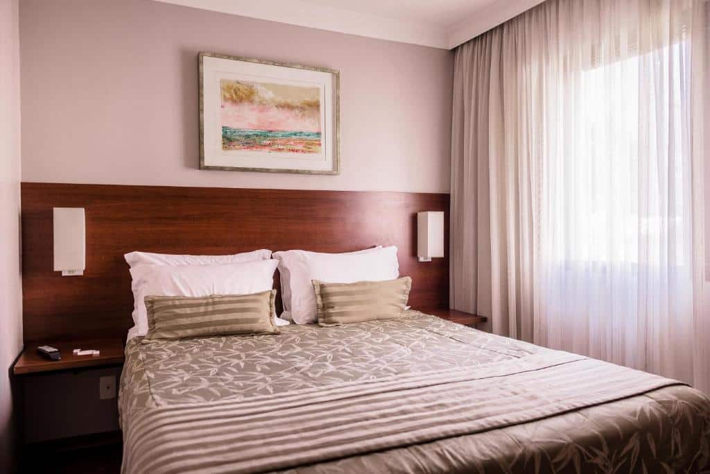 Uma cama bem arrumada com travesseiros listrados e uma colcha estampada em um quarto do hotel Matiz Manhattan com uma janela e arte na parede acima da cabeceira.