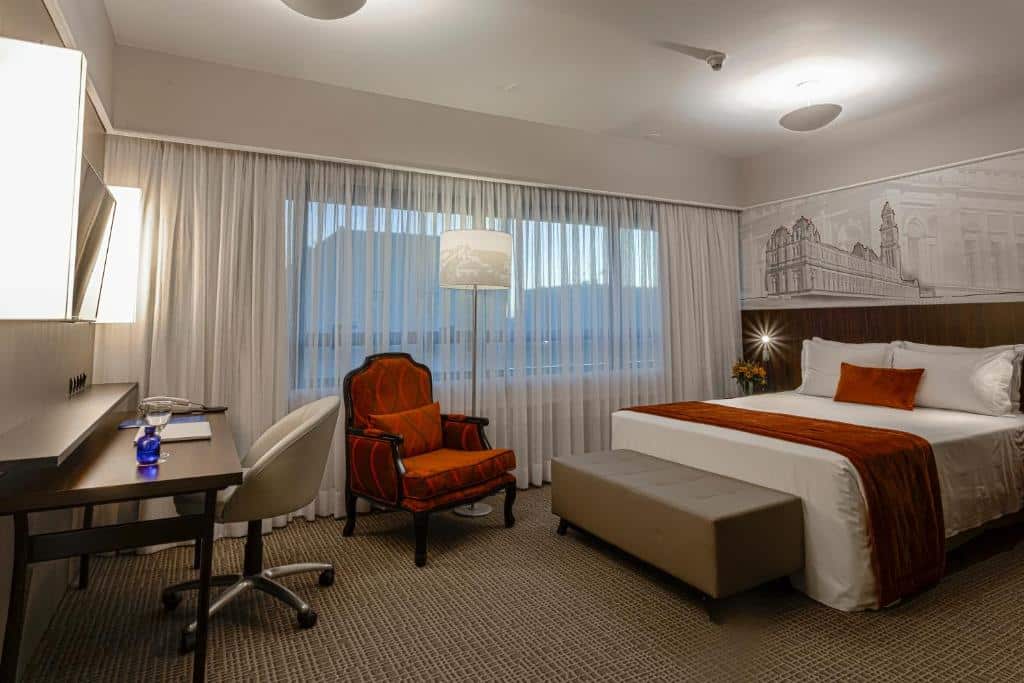Quarto amplo no Blue Tree Premium Paulista, com cama de casal, mesa de trabalho e poltrona vermelha