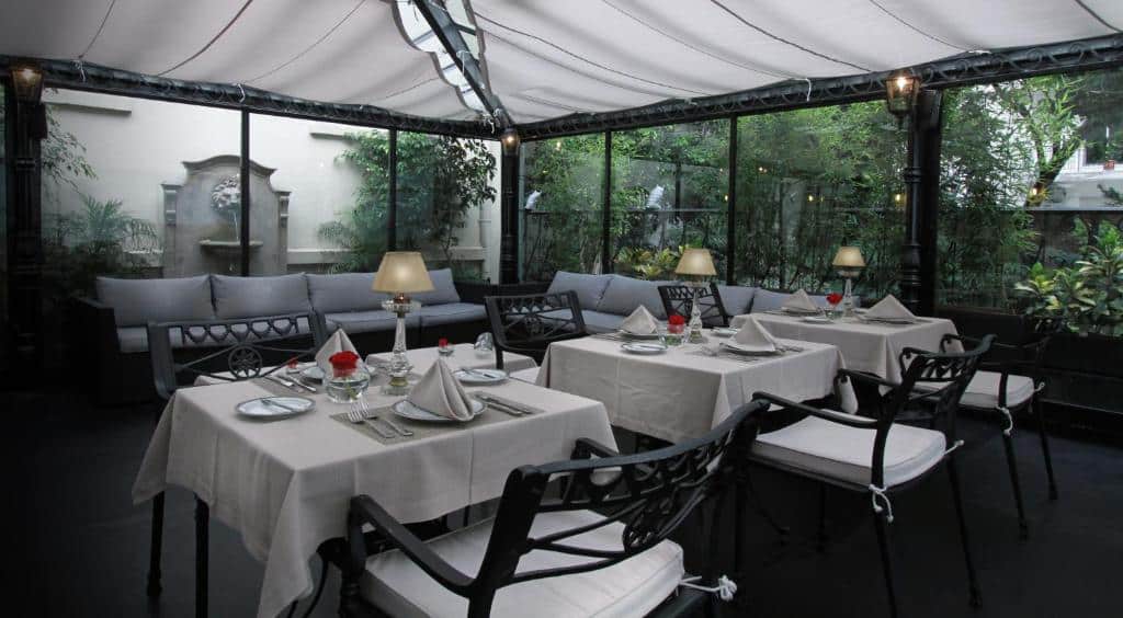 varanda do Melia Recoleta Plaza Hotel, um dos hotéis de luxo em Buenos Aires, com mesinha e cadeiras com paredes de vidro em que é possível ver a natureza ao redor e paredes históricas