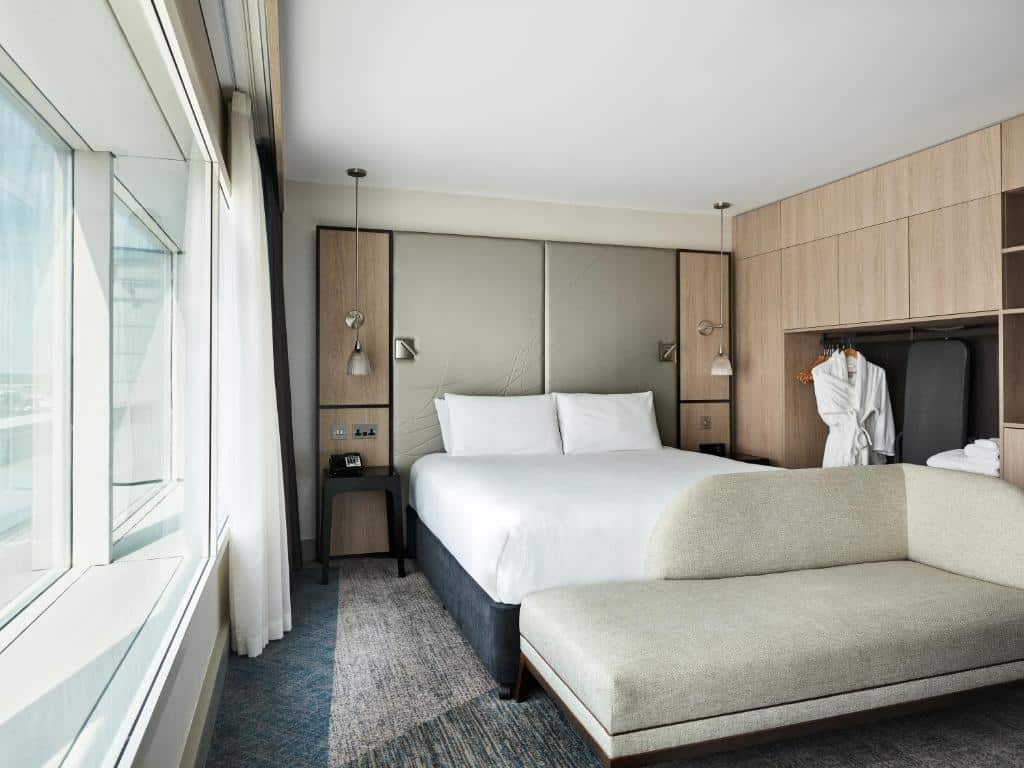 Quarto do Hyatt Place London Heathrow Airport com uma cama de casal, um sofá, janela ampla com cortinas e um armário