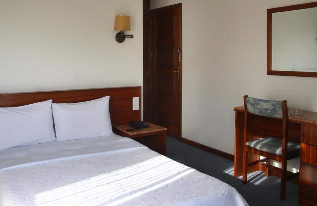 Quarto do Hotel Aeroporto com cama de casal do lado esquerdo da imagem e do lado direito da cama uma mesa de trabalho com cadeira. Representa hotéis perto do aeroporto do Porto.