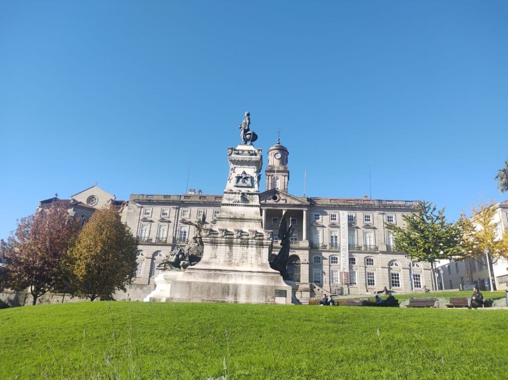 Imagem do Jardim do Infante Dom Henrique durante o dia com uma estatua a frente e ao fundo uma residência.