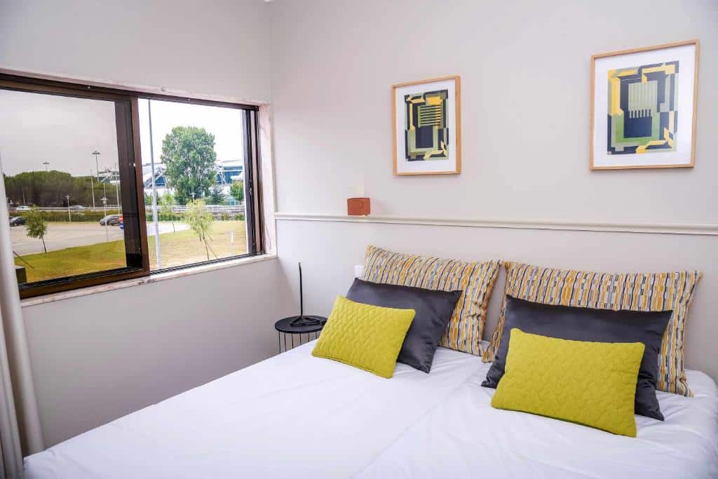 Quarto do Hotel Singular Porto Aeroporto com cama de casal do lado direito e uma mesa com luminária do lado esquerdo da cama. Representa hotéis perto do aeroporto do Porto.