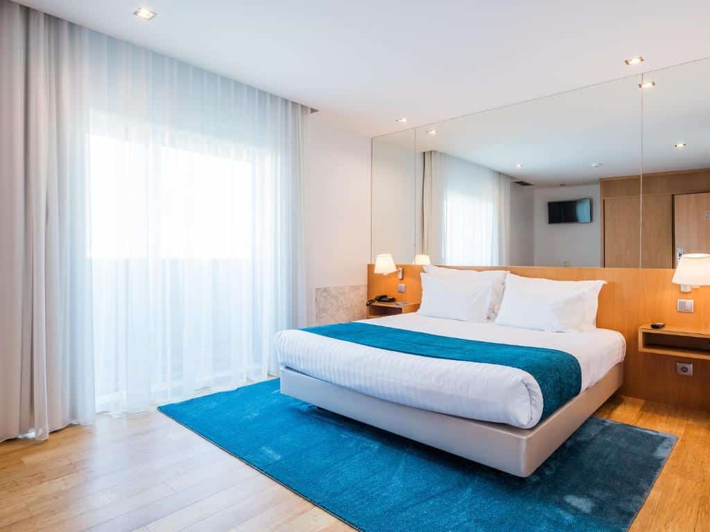 Quarto do OPOHOTEL Porto Aeroporto com cama de casal do lado direito com duas luminárias na cabeceira da cama. Representa hotéis perto do aeroporto do Porto.