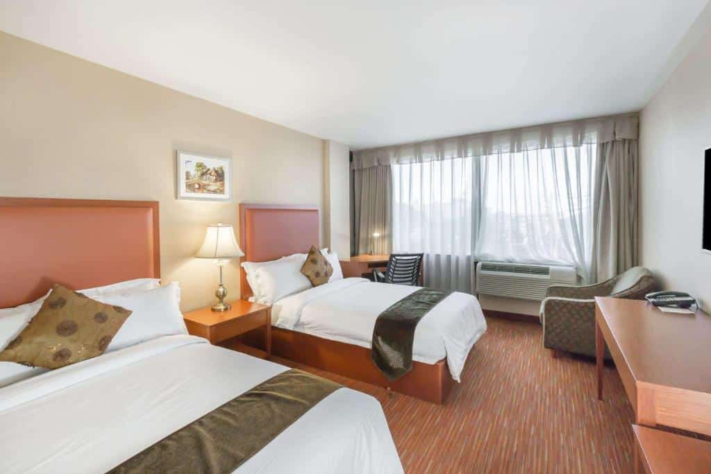 duas camas de casal do Ramada by Wyndham Flushing Queens com uma mesa para trabalho no canto esquerdo. Já no canto direito há uma pequena poltrona estofada e estampada