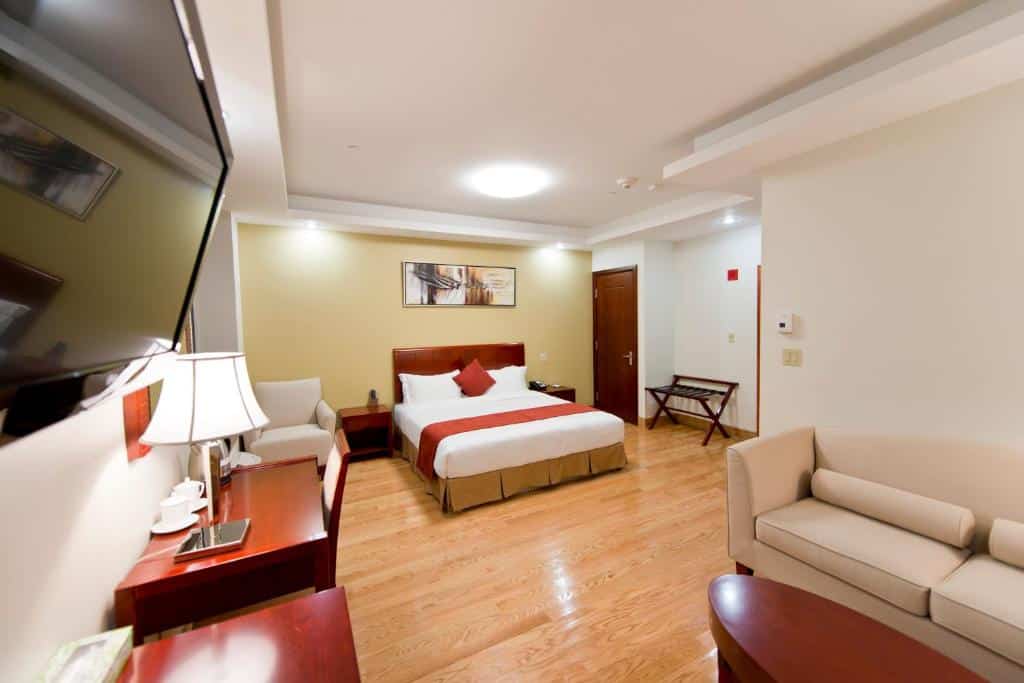 suíte do Asiatic Hotel, um dos hotéis perto do aeroporto laguardia em nova york, com uma cama de casal ao fundo, uma poltrona clara ao lado, um sofá de dois lugares mais a frente, à direita, encostado à parede, e uma televisão pequena presa a parede contrária, de frente para o sofá