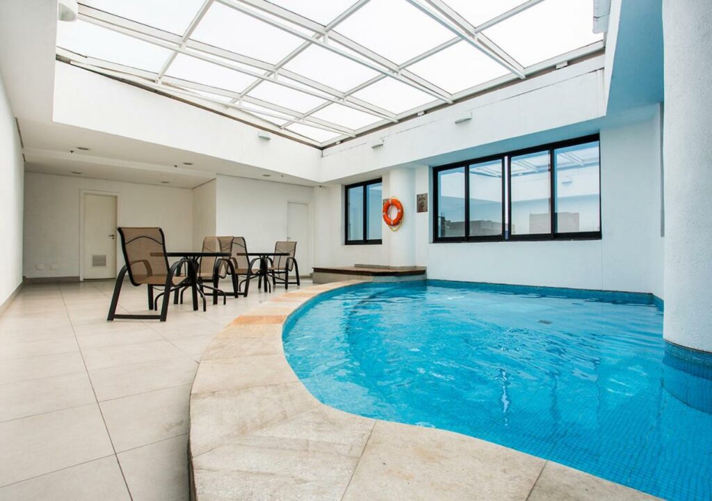 Piscina coberta com teto de vidro no Estanplaza Berrini com um pequeno deck ao redor com mesas e cadeiras