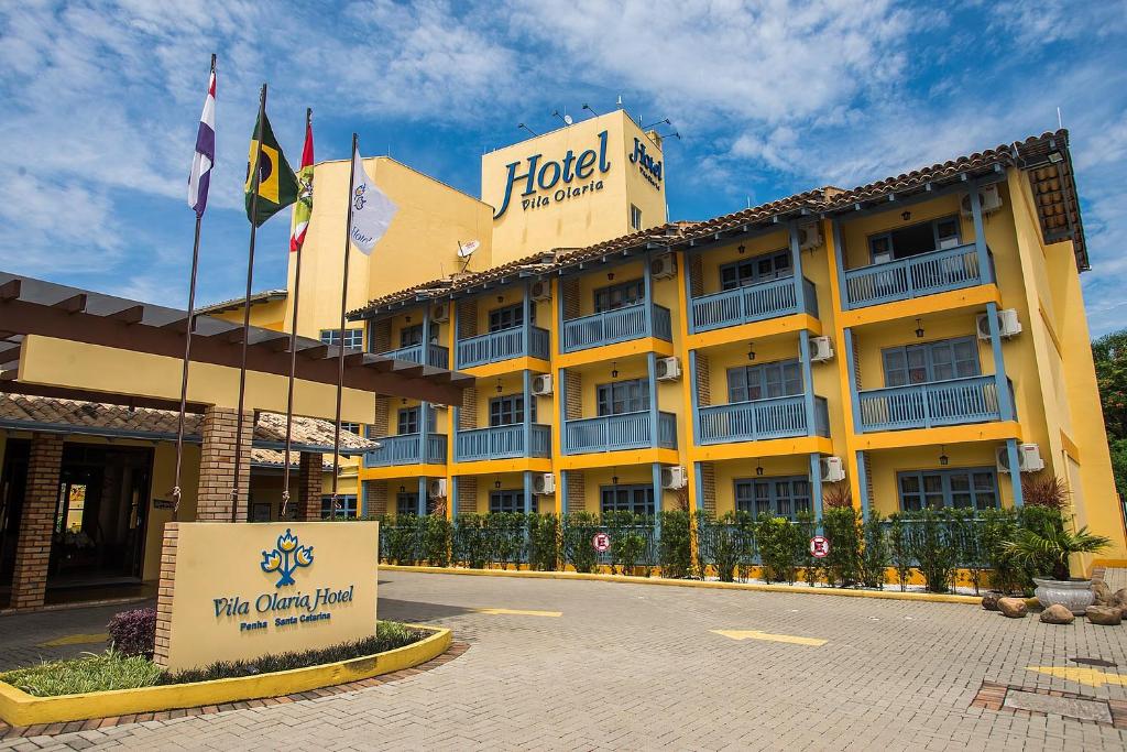 Fachada do Vila Olaria Hotel, com paredes amarelas e sacadas com parapeito azul e caixa de ar-condicionado