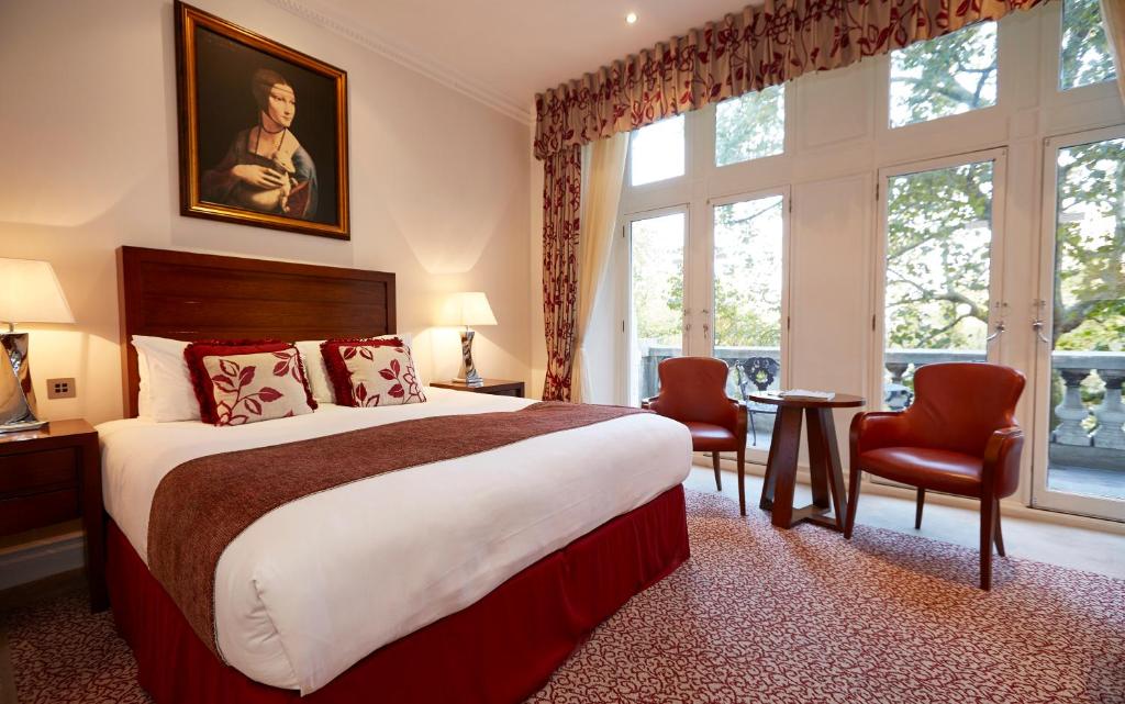 Quarto do The Royal Horseguards com uma ssacada com portas de vidro, carpete vermelho e branco, cama de casal, itens de decoração e duas poltronas vermelhas