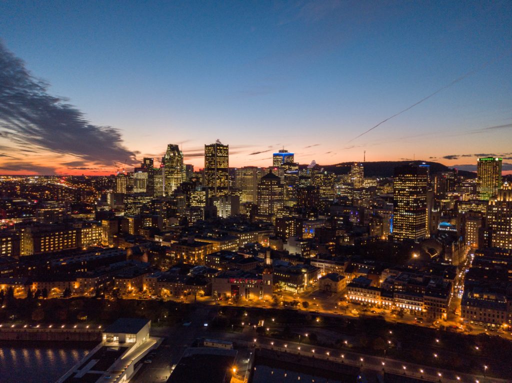 Vista aérea do horizonte de uma cidade ao anoitecer, com arranha-céus iluminados e um céu escuro com nuvens dispersas. A imagem ilustra o post sobre intercâmbio no Canadá.
