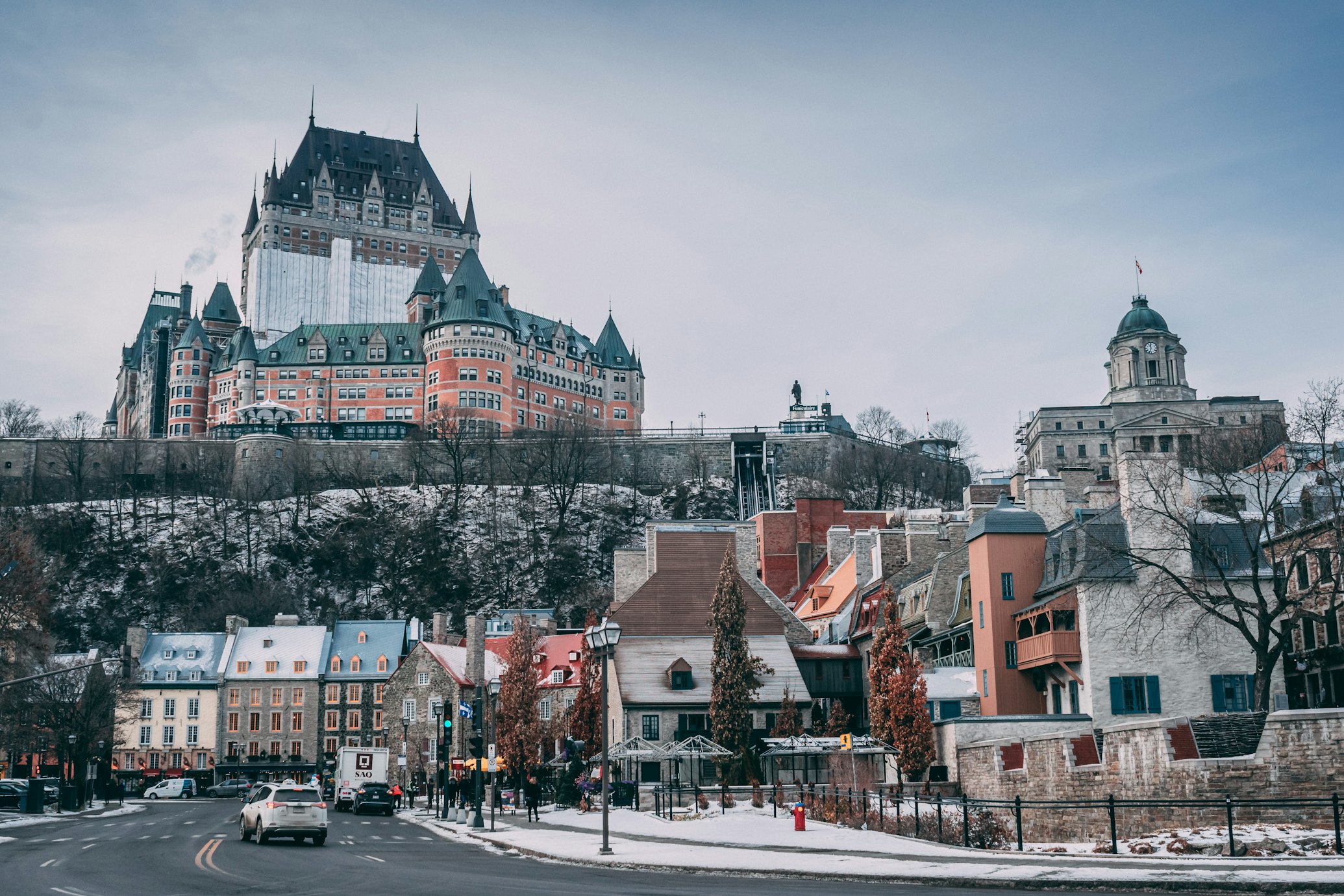 Uma vista panorâmica da Velha Quebec, mostrando o Château Frontenac no topo de uma colina e edifícios históricos abaixo, com neve leve no chão. A imagem ilustra o post sobre intercâmbio no Canadá.
