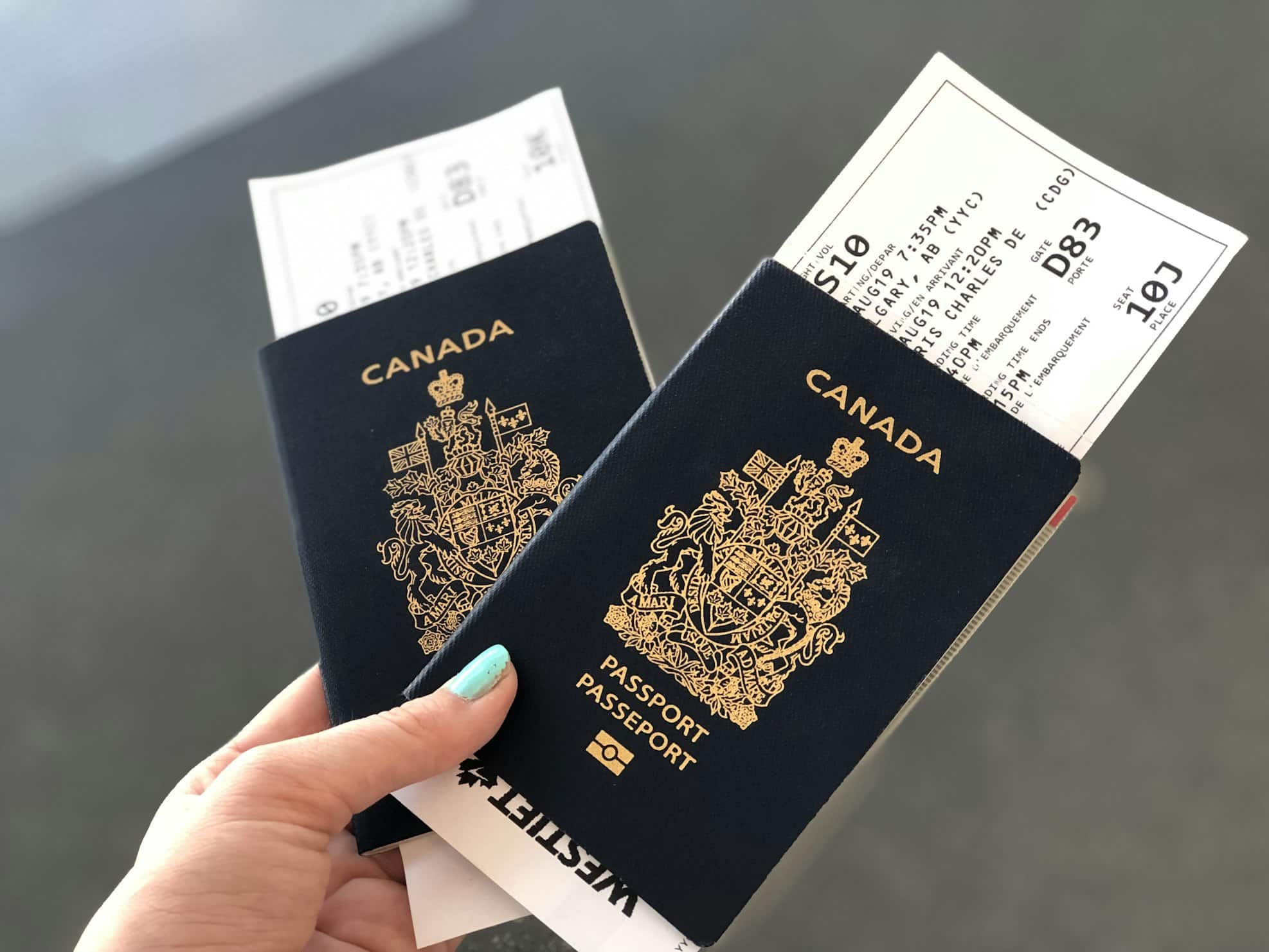 Uma mão segura dois passaportes canadenses, cada um com um cartão de embarque visível dentro, contra um fundo desfocado.
