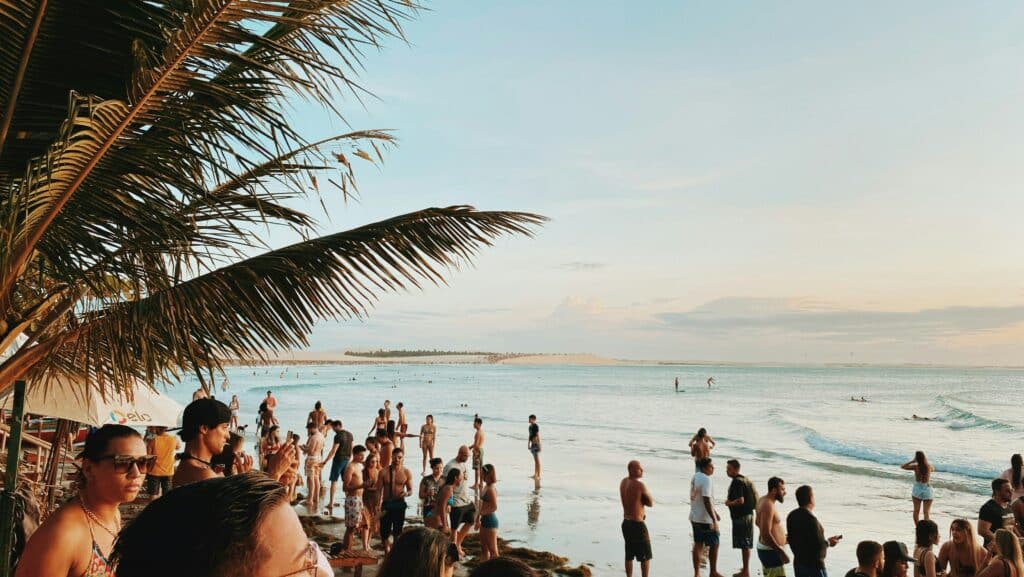 Imagem da Praia de Jeri, onde há várias pessoas conversando perto do mar. Outras estão nadando.
