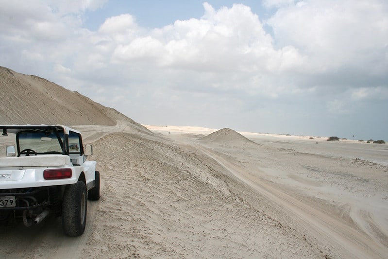Um buggy branco está na esquerda da foto, sobre as dunas. A foto representa o post sobre o que fazer em Jericoacoara.